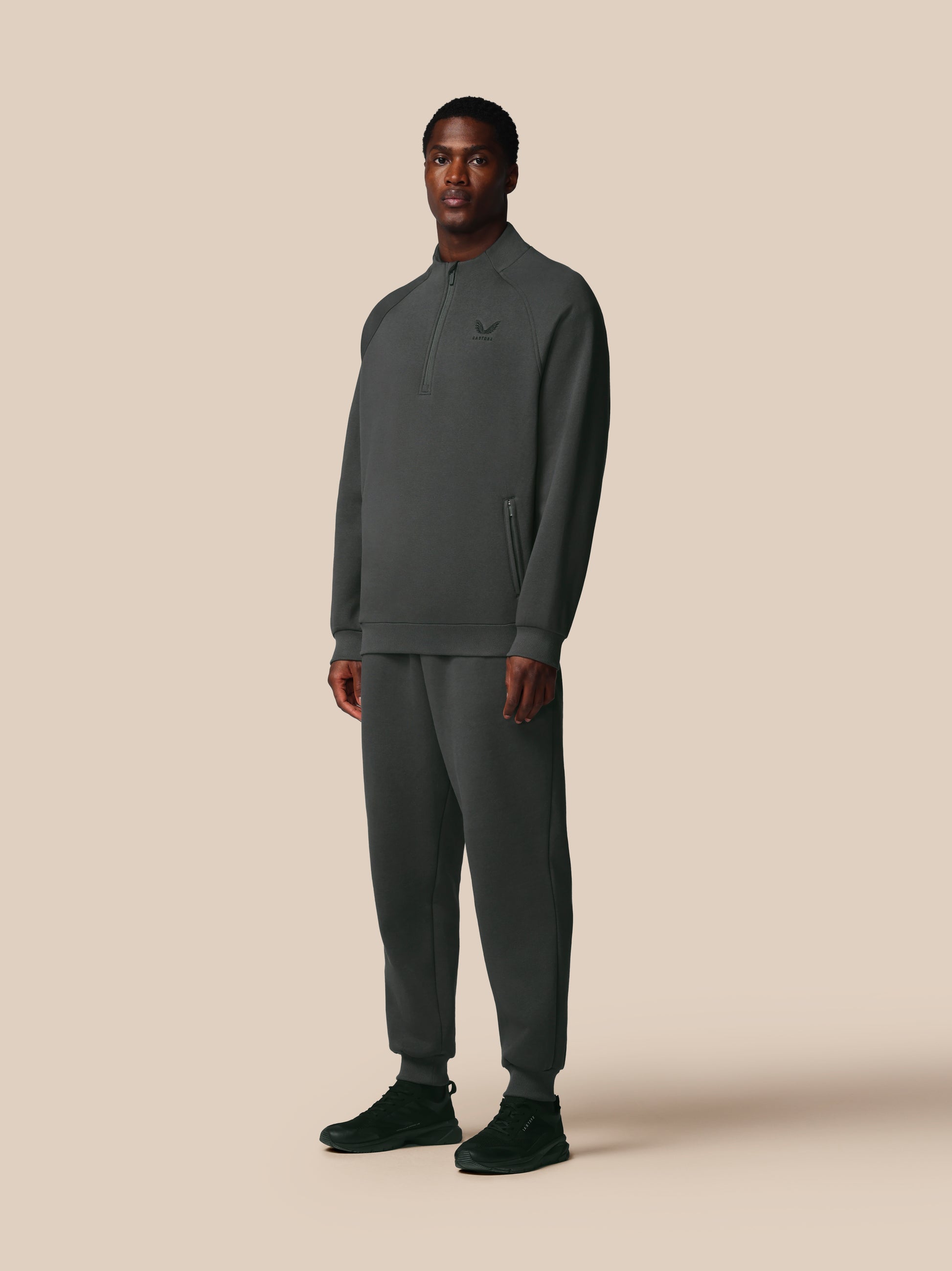 Man wearing a dark gray Castore tracksuit on a beige background