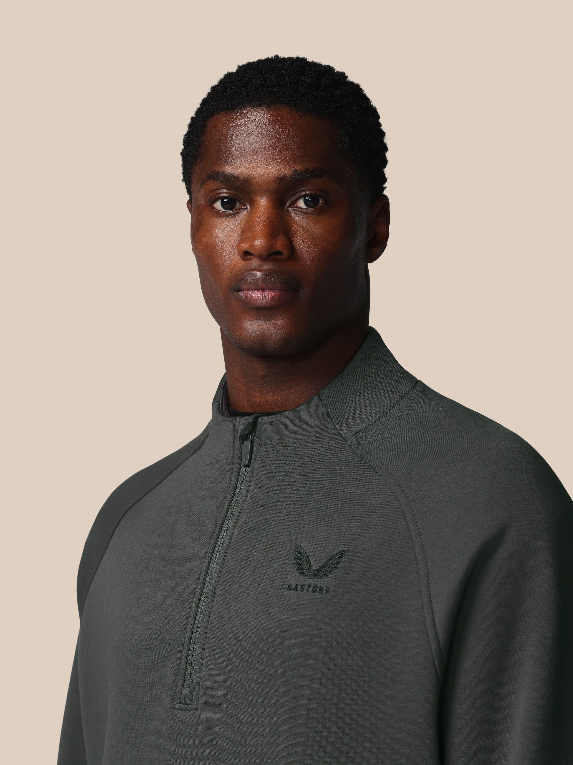 Man wearing a dark gray pullover with a logo on a beige background