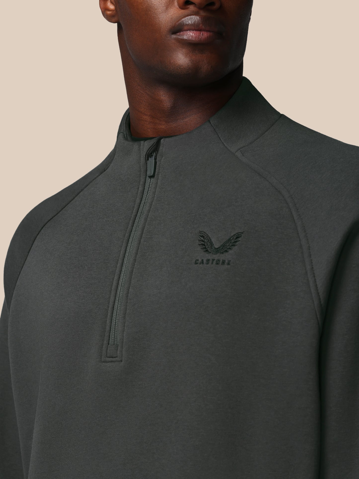 Man wearing a dark gray quarter-zip sweatshirt with a brand logo on a beige background