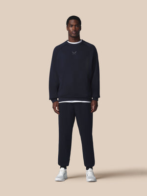 Man wearing a navy blue sweatshirt and pants with white sneakers on a beige background