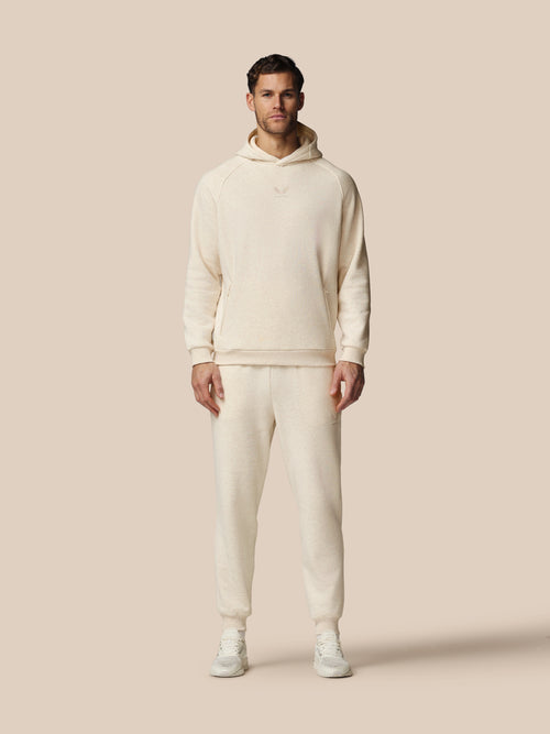 Man wearing a cream-colored hoodie and pants on a beige background