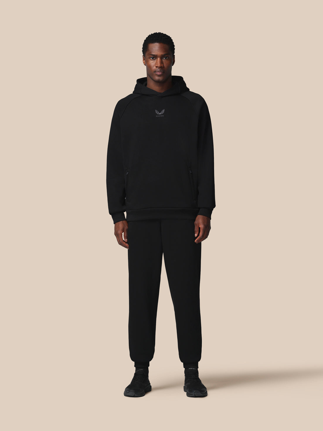 Person wearing a black hoodie and pants on a beige background