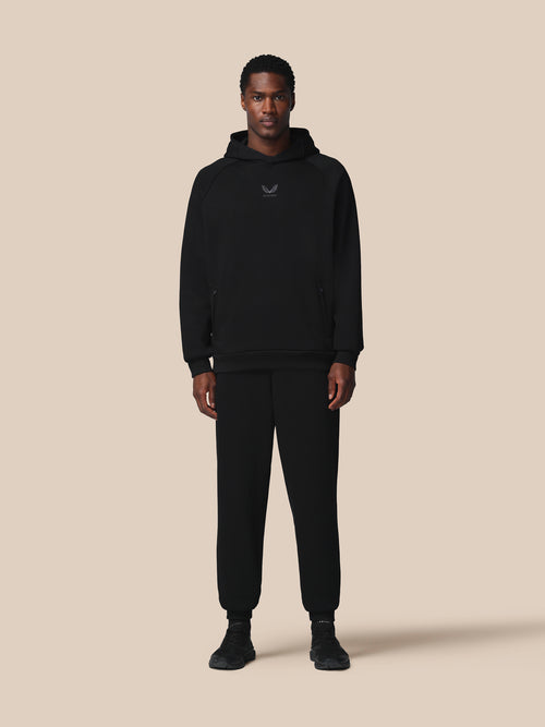 Person wearing a black hoodie and pants on a beige background
