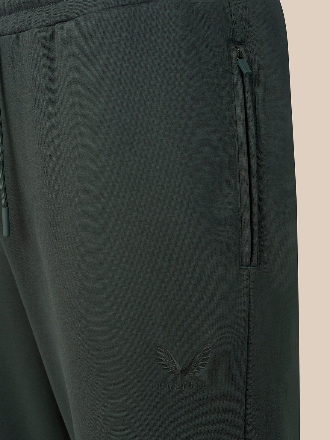 Close-up of dark gray sweatpants showing a side zip pocket, drawstring waistband, and a tonal embroidered winged logo near the lower leg.
