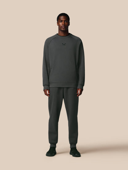 Man wearing a dark gray sweatshirt and pants on a beige background