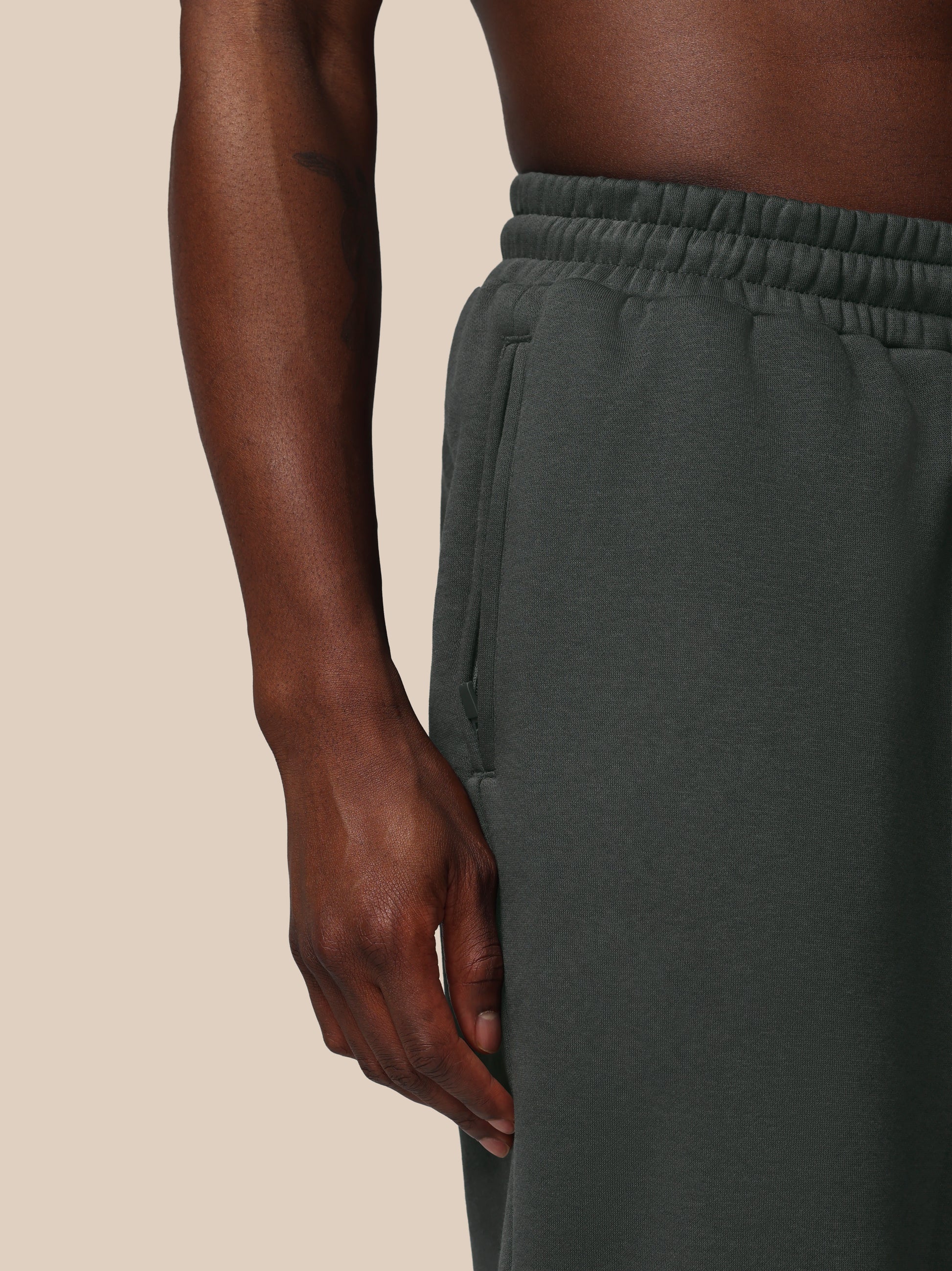 Dark green sweatpants worn by a person on a beige background