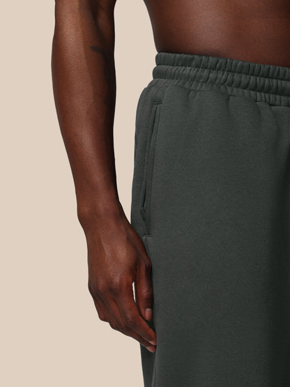 Dark green sweatpants worn by a person on a beige background