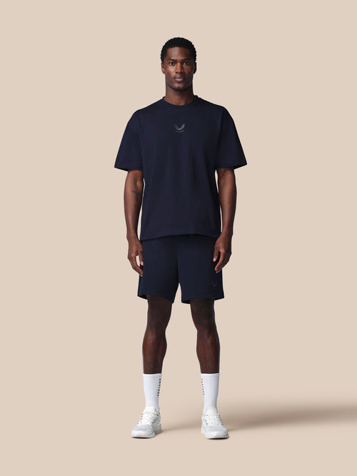 Man wearing a navy t-shirt and shorts set with white socks and shoes on a beige background