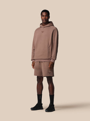 Man wearing a brown hoodie and shorts set on a beige background