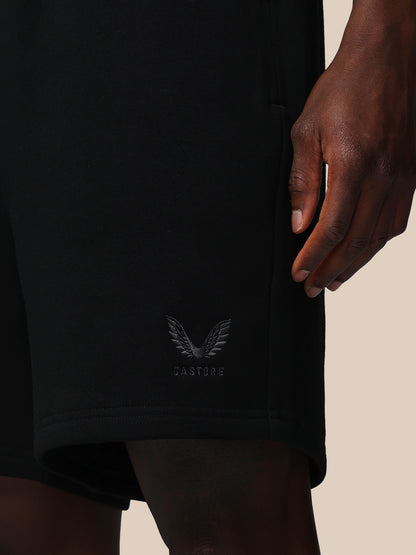 Black shorts with a logo on the waistband against a beige background