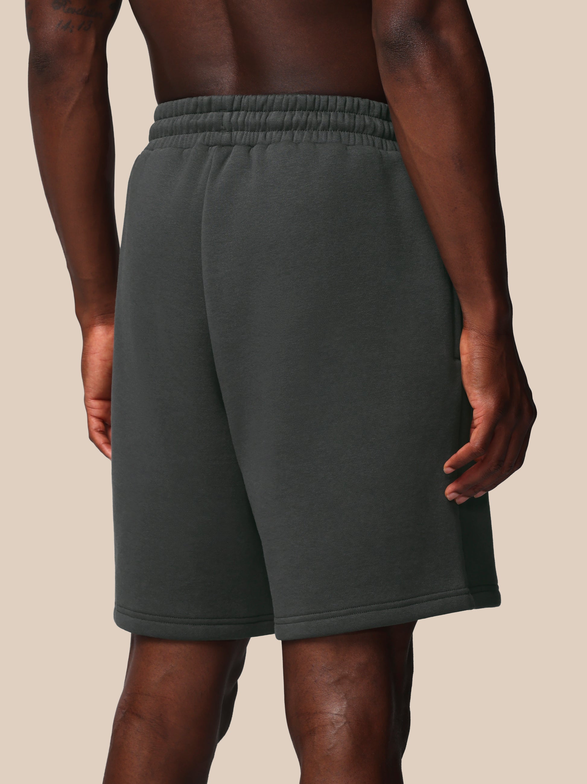 Person wearing dark gray sweat shorts on a beige background