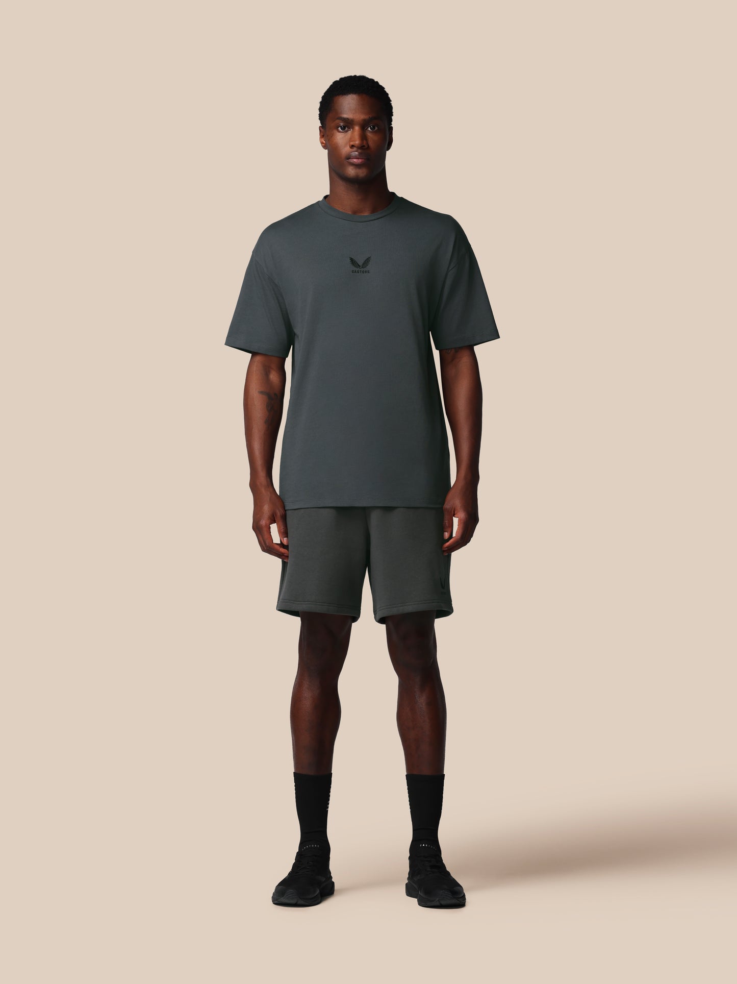 Man wearing a dark gray t-shirt and shorts set on a beige background