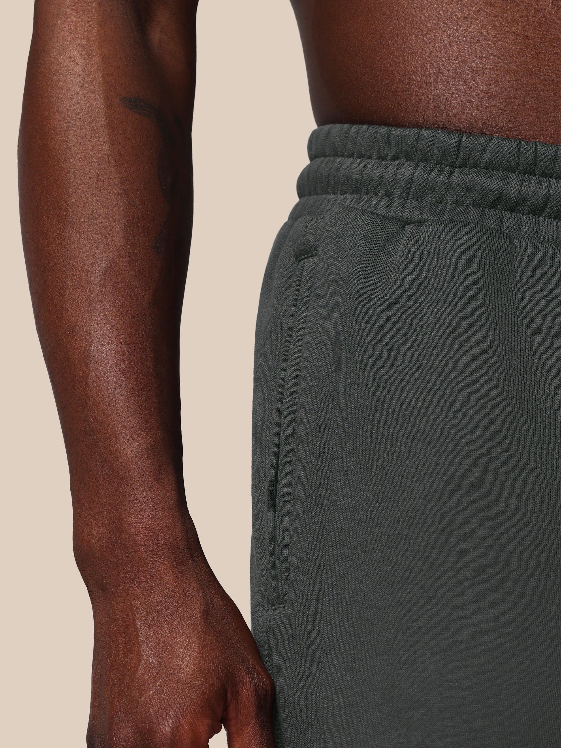 Person wearing dark green sweatpants on a beige background