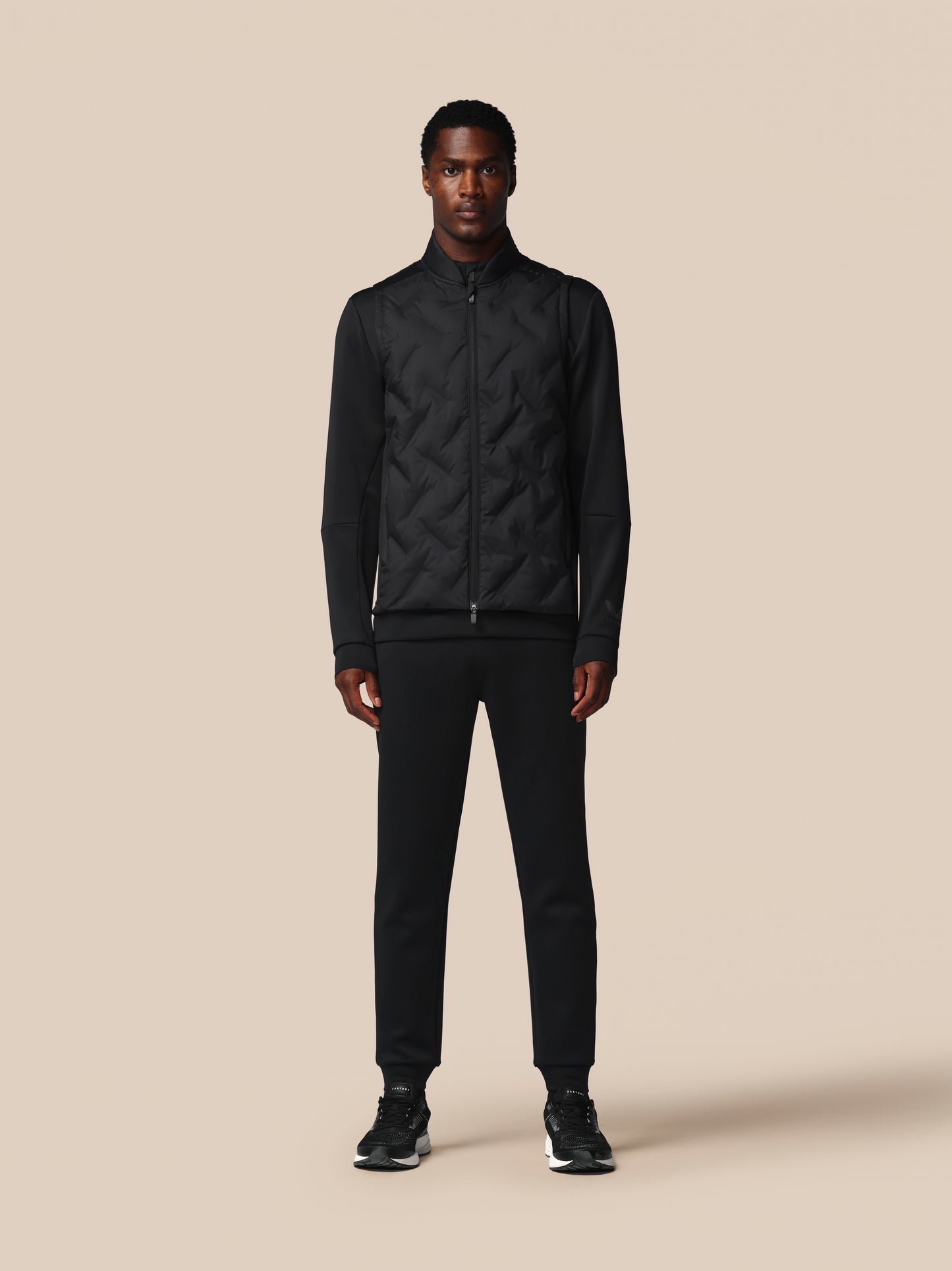 Man wearing a black quilted jacket and pants on a beige background
