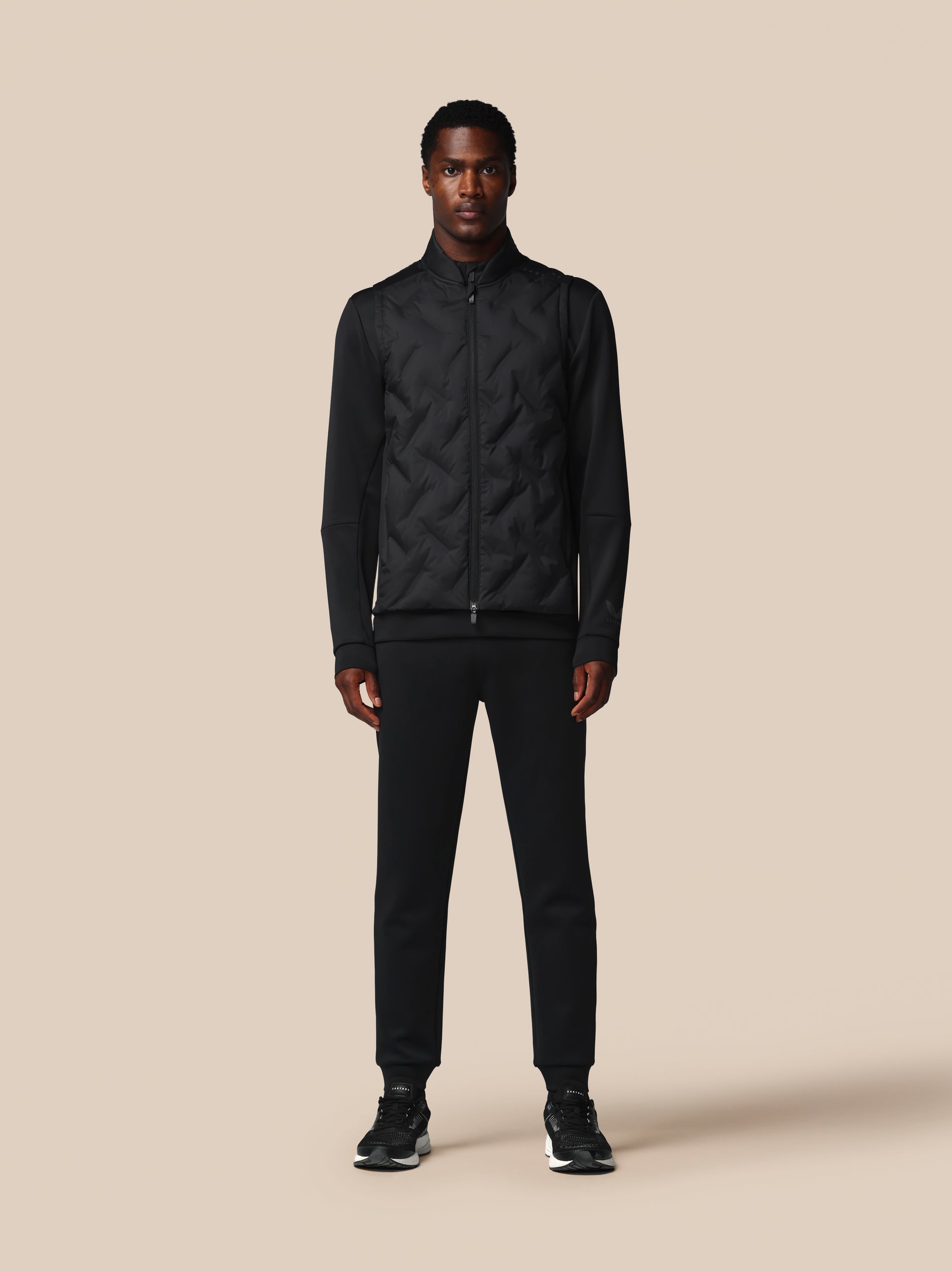 Man wearing a black quilted jacket and pants on a beige background