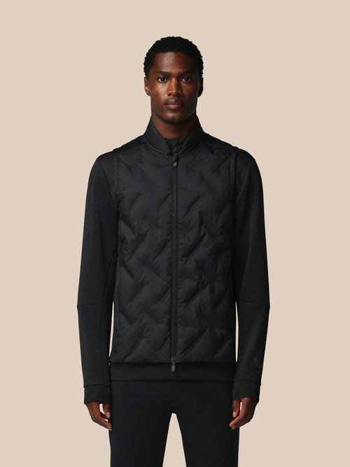 Man wearing a black quilted jacket against a beige background