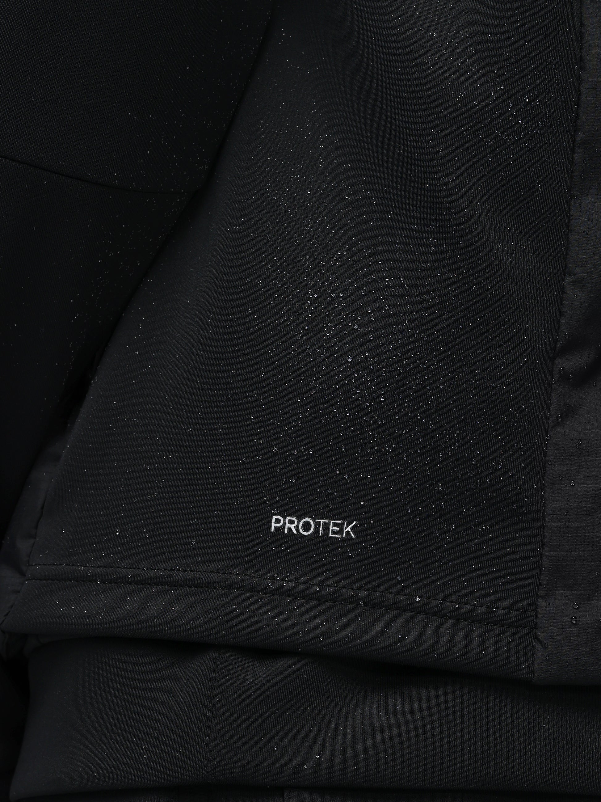 Close-up of a black jacket with 'PROTEK' branding on a dark background