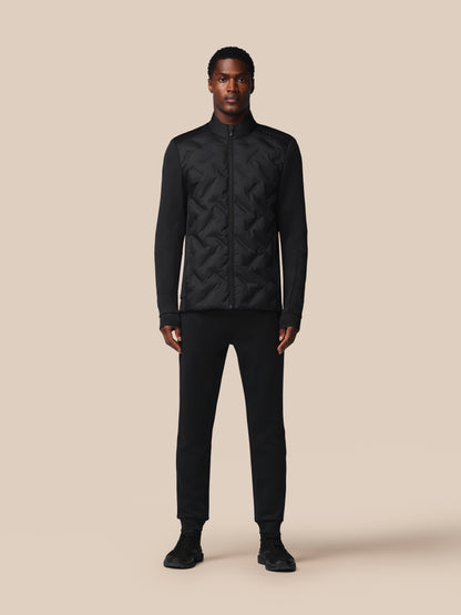 Man wearing a black quilted jacket and pants on a beige background