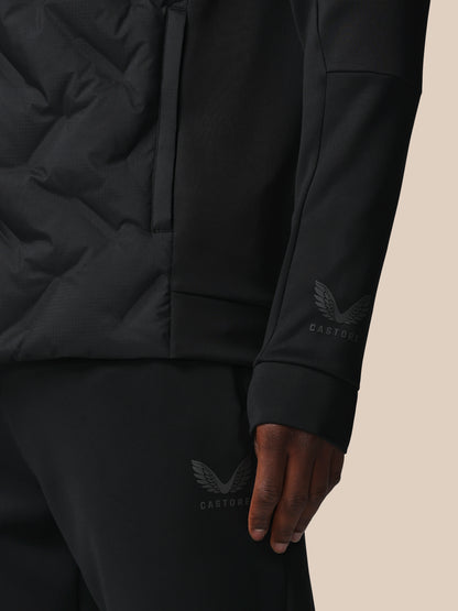 Close-up of a person wearing a black jacket and pants with a brand logo on a beige background