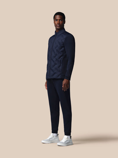Man wearing a navy quilted jacket and pants with white sneakers on a beige background