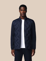 Man wearing a navy quilted jacket over a white shirt on a beige background