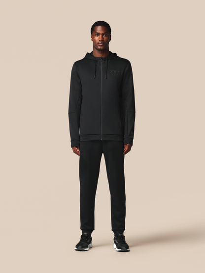 Person wearing a black hoodie and pants on a beige background