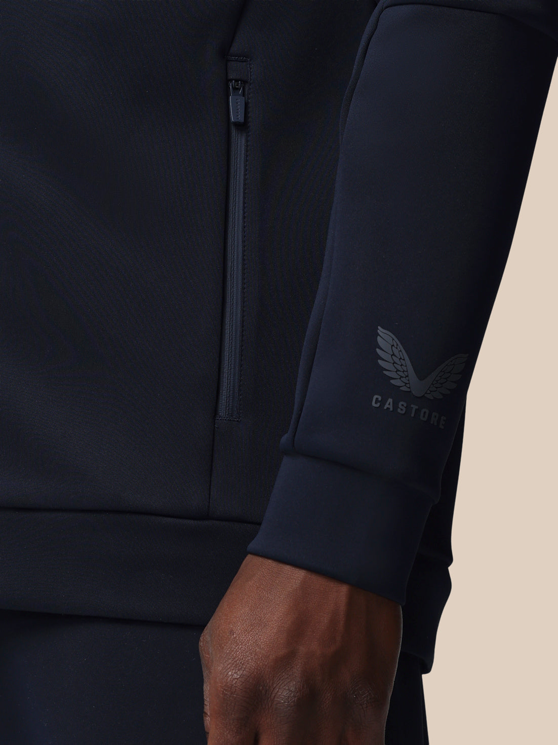 Close-up of a dark blue athletic jacket with a brand logo on the sleeve against a beige background