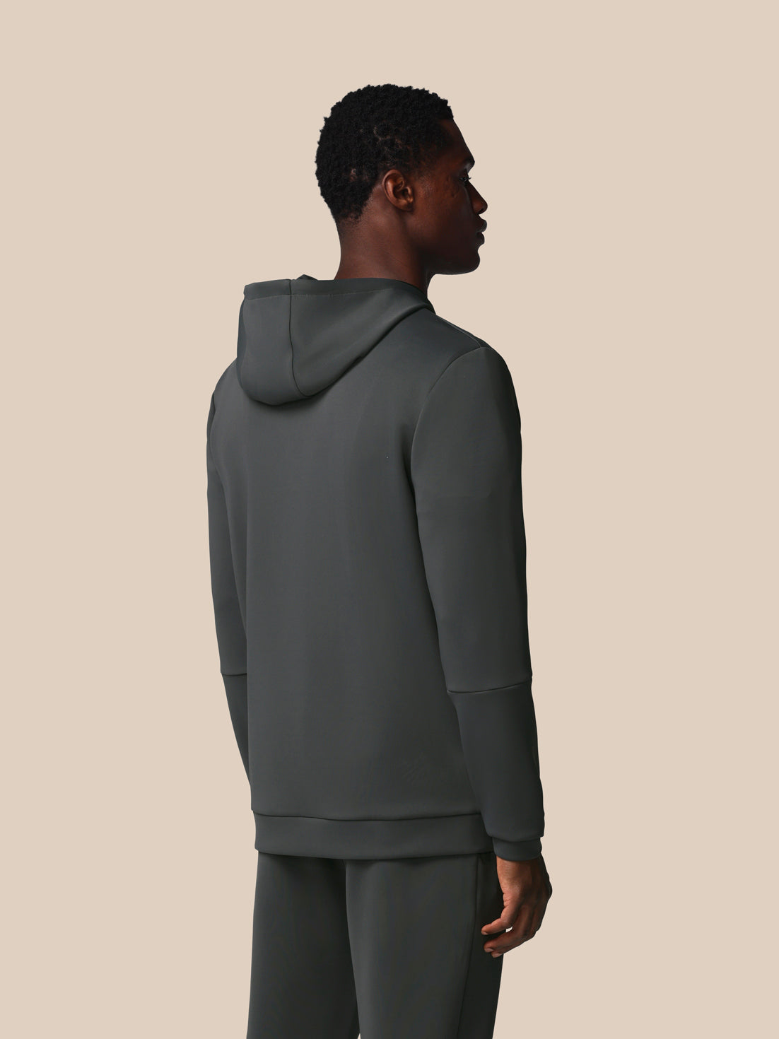 Person wearing a dark gray hoodie and pants on a beige background