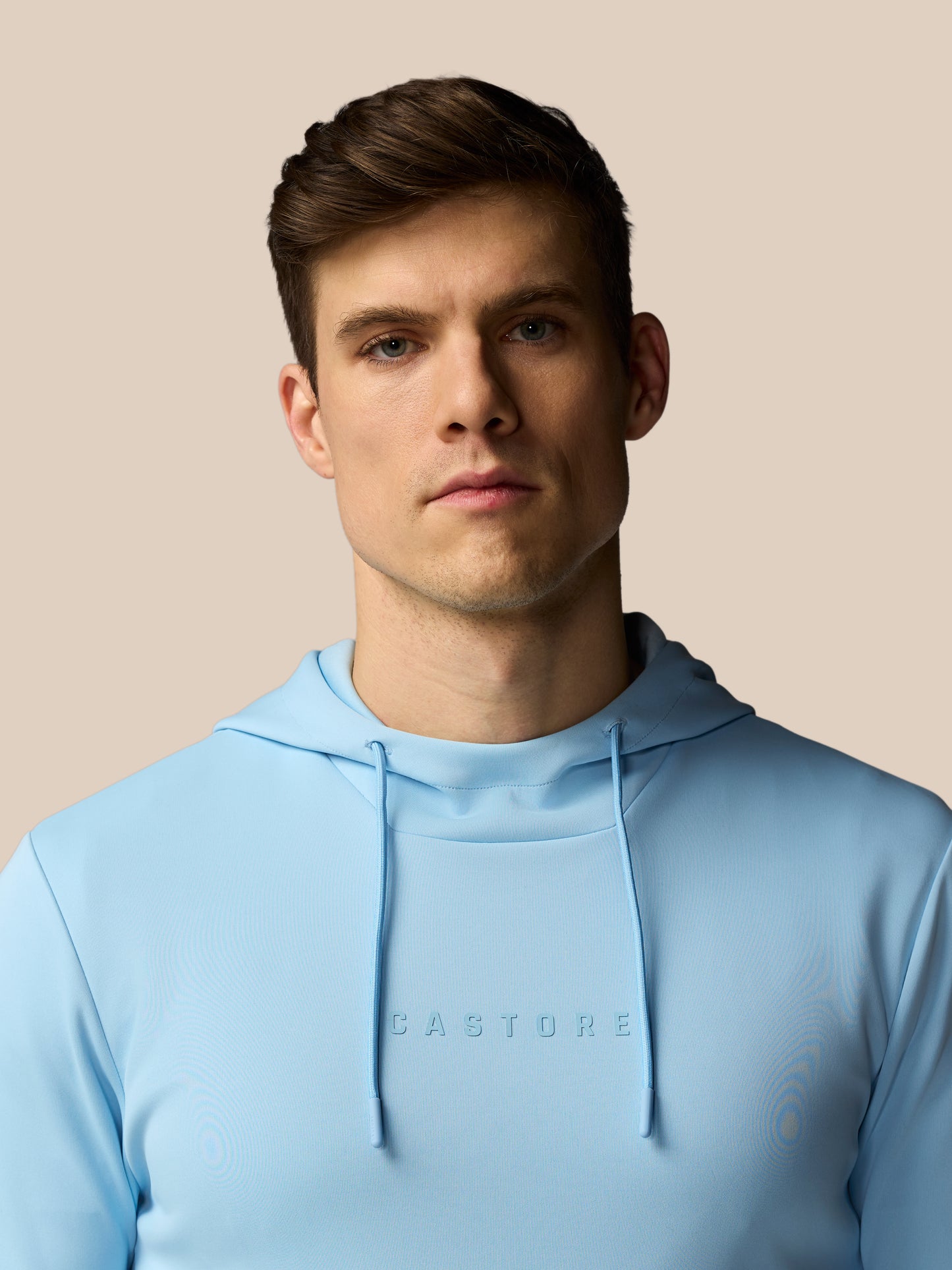 Man wearing a light blue hoodie with 'CASTORE' branding against a beige background