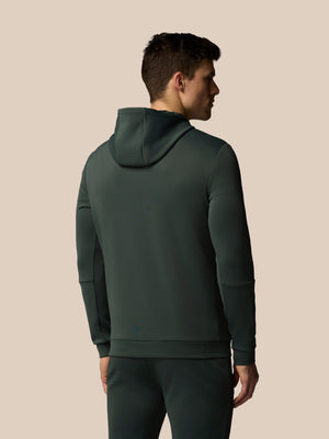 Man wearing a dark green hoodie and pants on a beige background