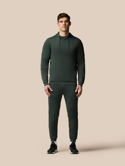 Man wearing a dark green hoodie and jogger pants on a beige background