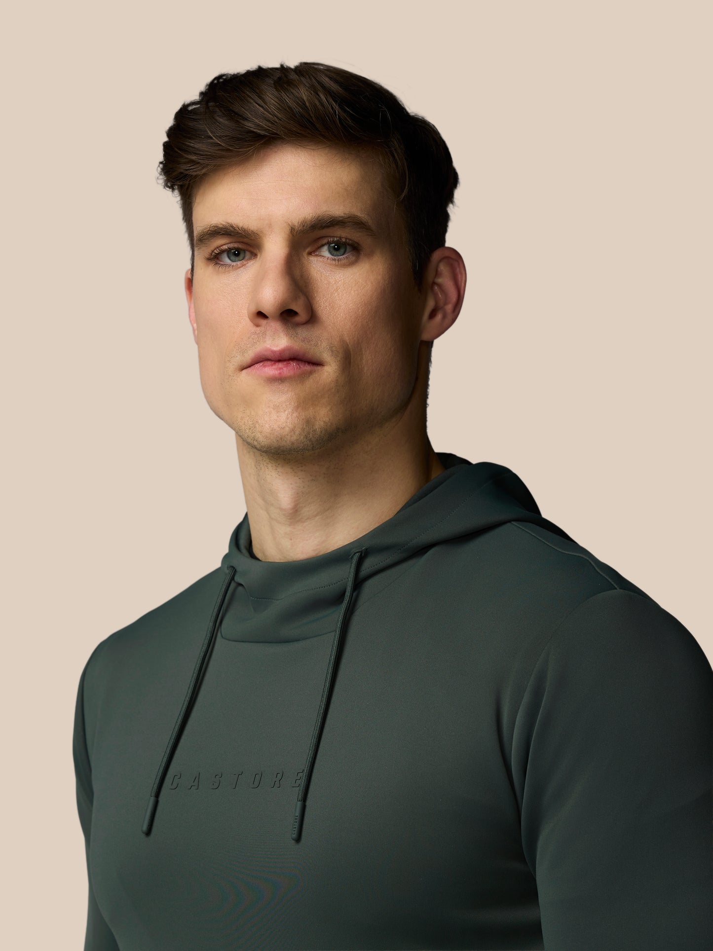 Man wearing a dark green hoodie against a beige background