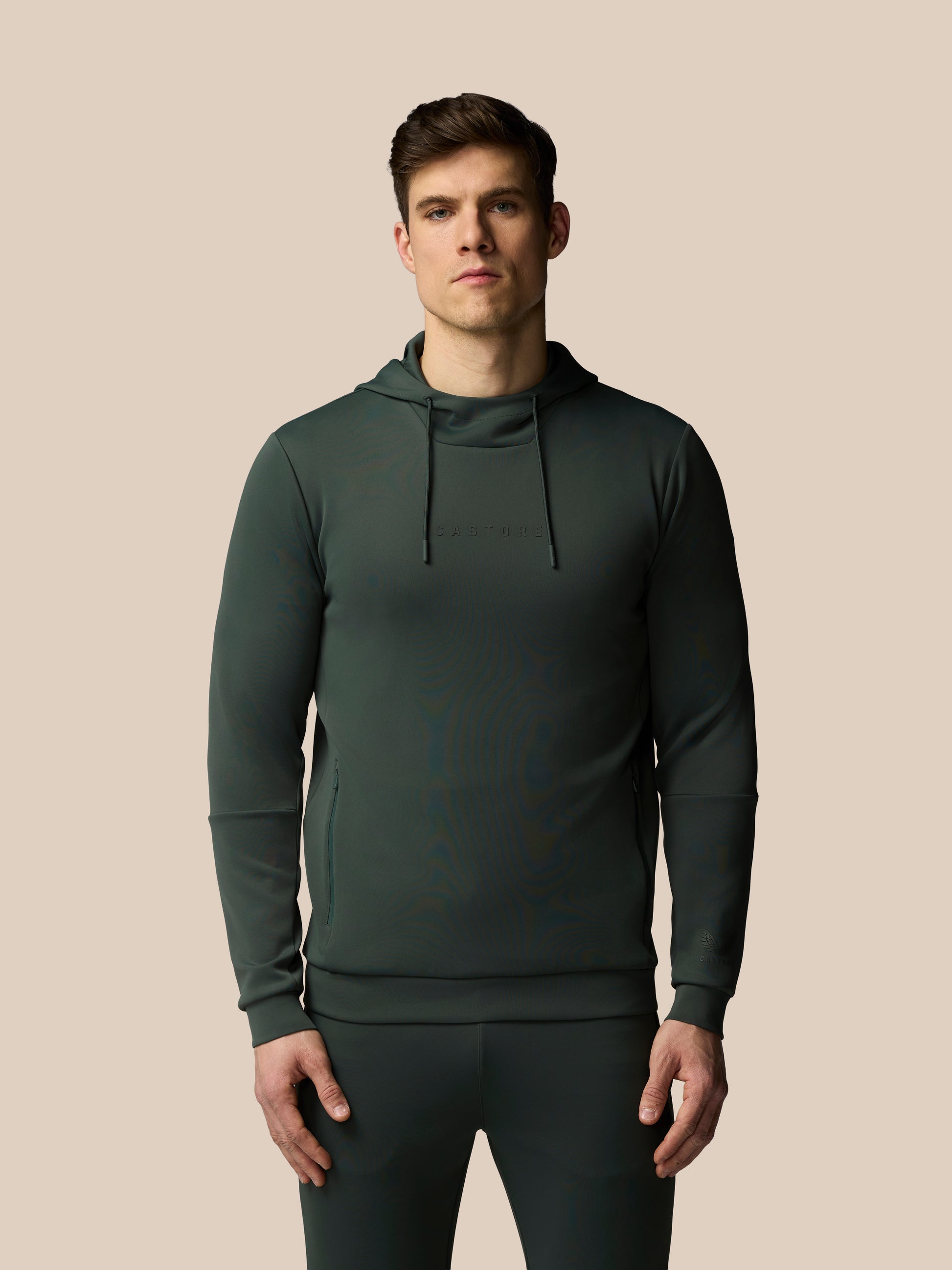 Man wearing a dark green hoodie and pants on a beige background