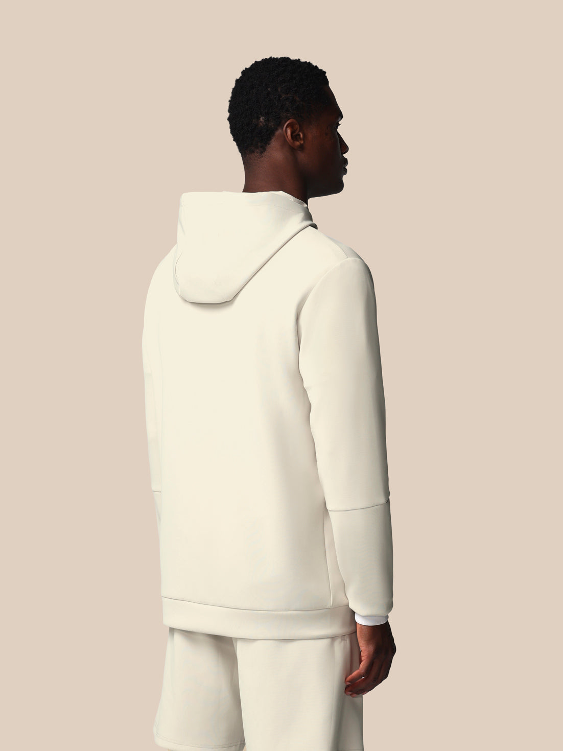 Person wearing a cream-colored hoodie and pants on a beige background