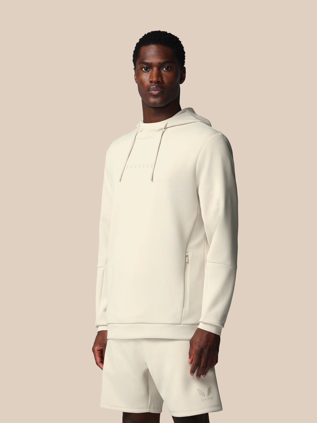 Man wearing a white hoodie and shorts set against a beige background