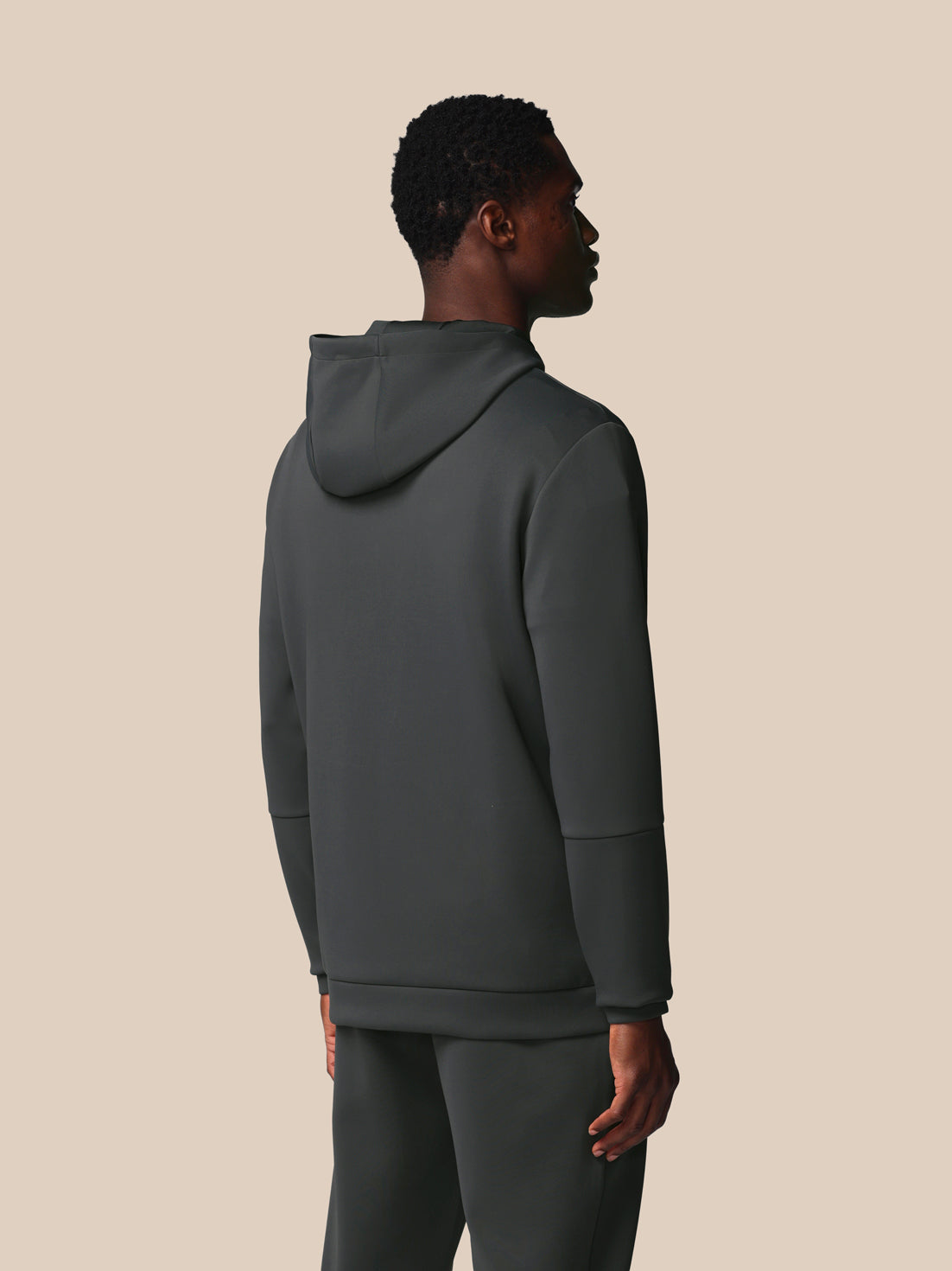 Person wearing a dark gray hoodie and pants on a beige background