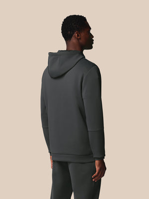 Person wearing a dark gray hoodie and pants on a beige background