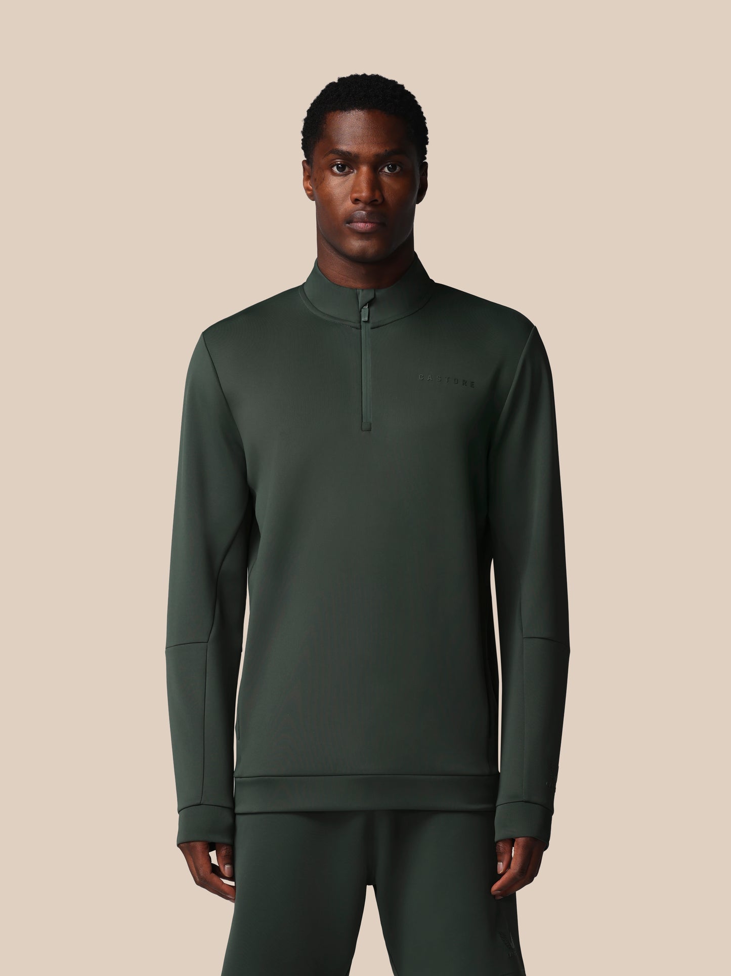 Man wearing a dark green long-sleeve shirt with a quarter zip on a beige background