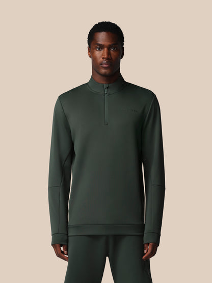 Man wearing a dark green long-sleeve shirt with a quarter zip on a beige background