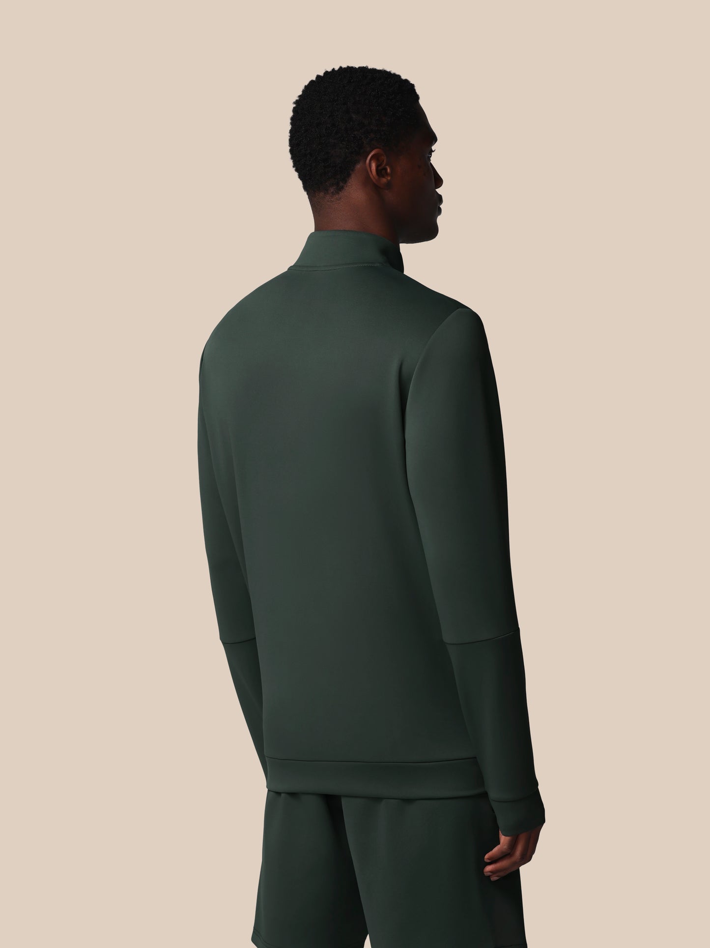Person wearing a dark green tracksuit against a beige background