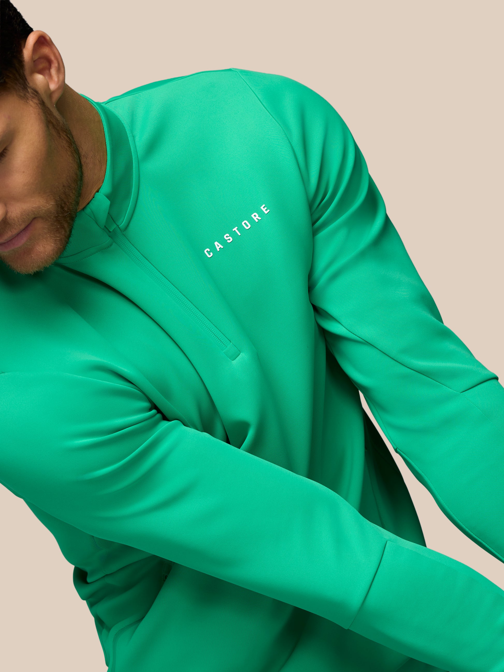 Person wearing a green long-sleeve shirt with 'Castore' branding on a beige background
