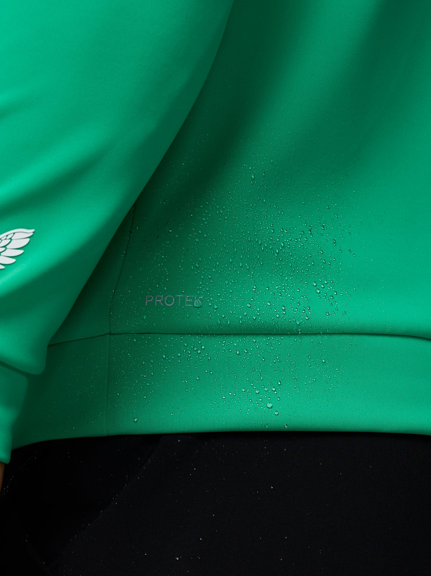 Close-up of a green jacket with water droplets on the fabric, featuring a brand logo.