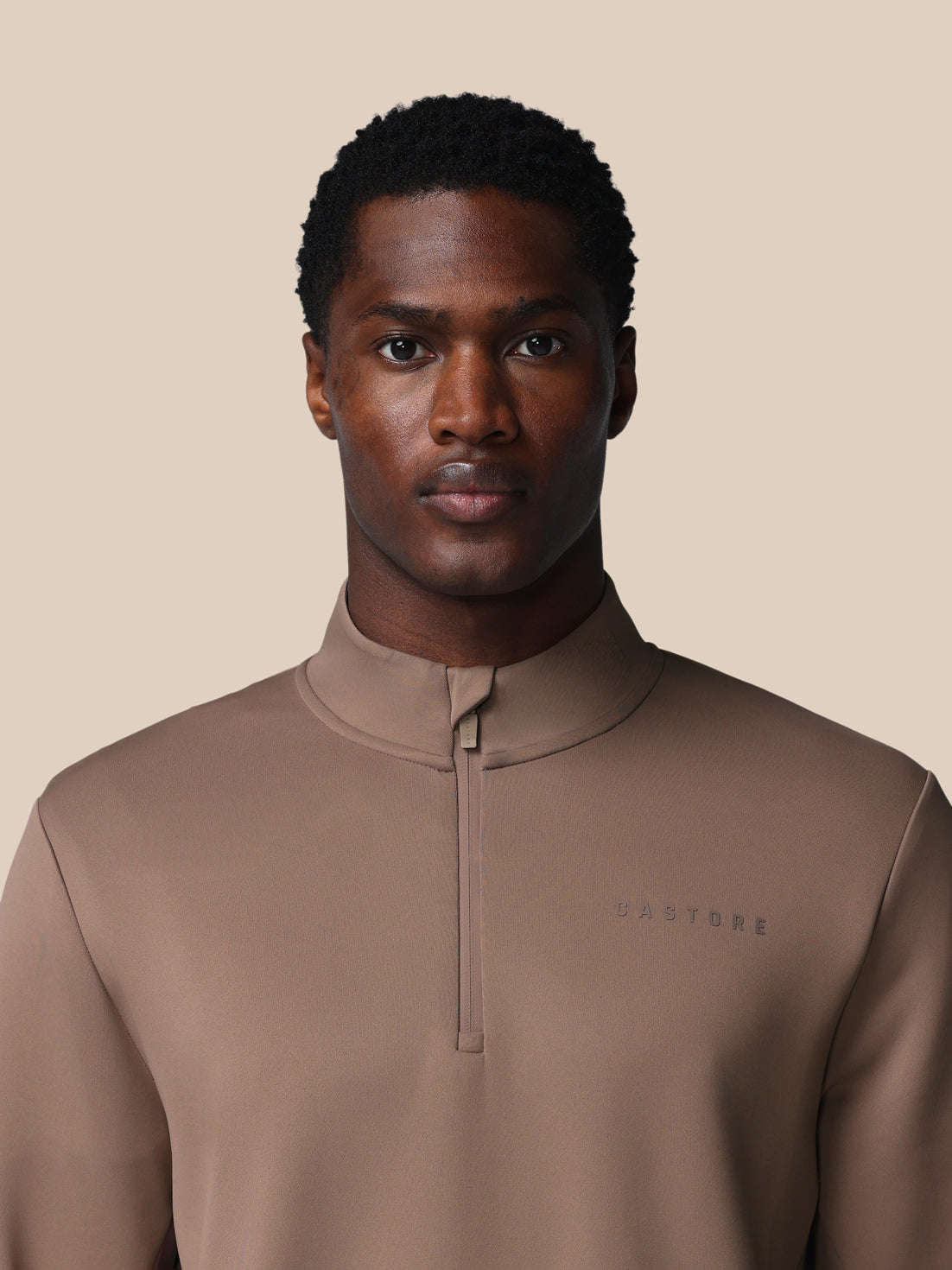 Man wearing a brown quarter-zip pullover against a beige background