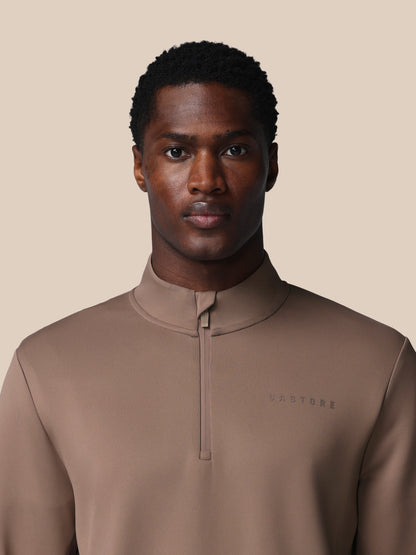 Man wearing a brown quarter-zip pullover against a beige background