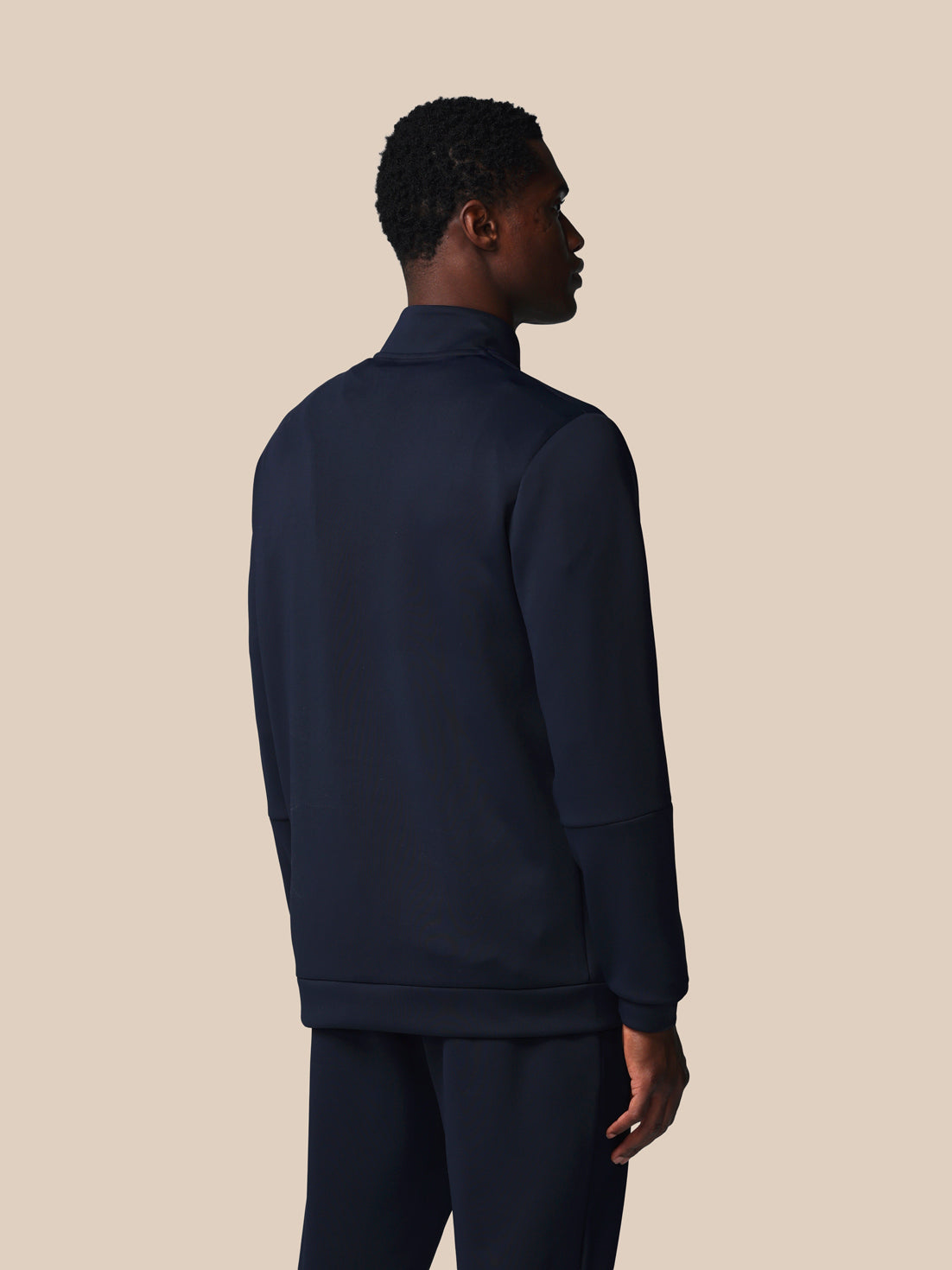 Person wearing a navy blue tracksuit against a beige background