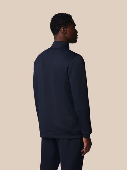 Person wearing a navy blue tracksuit against a beige background