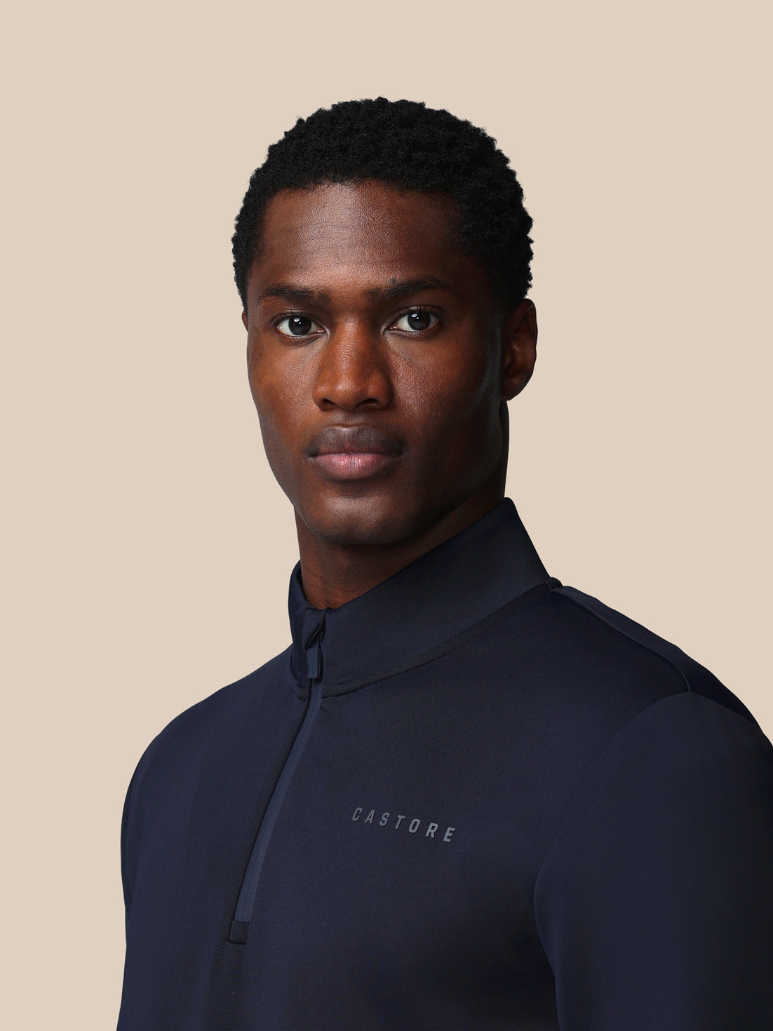 Man wearing a navy blue jacket with 'Castore' branding on a beige background