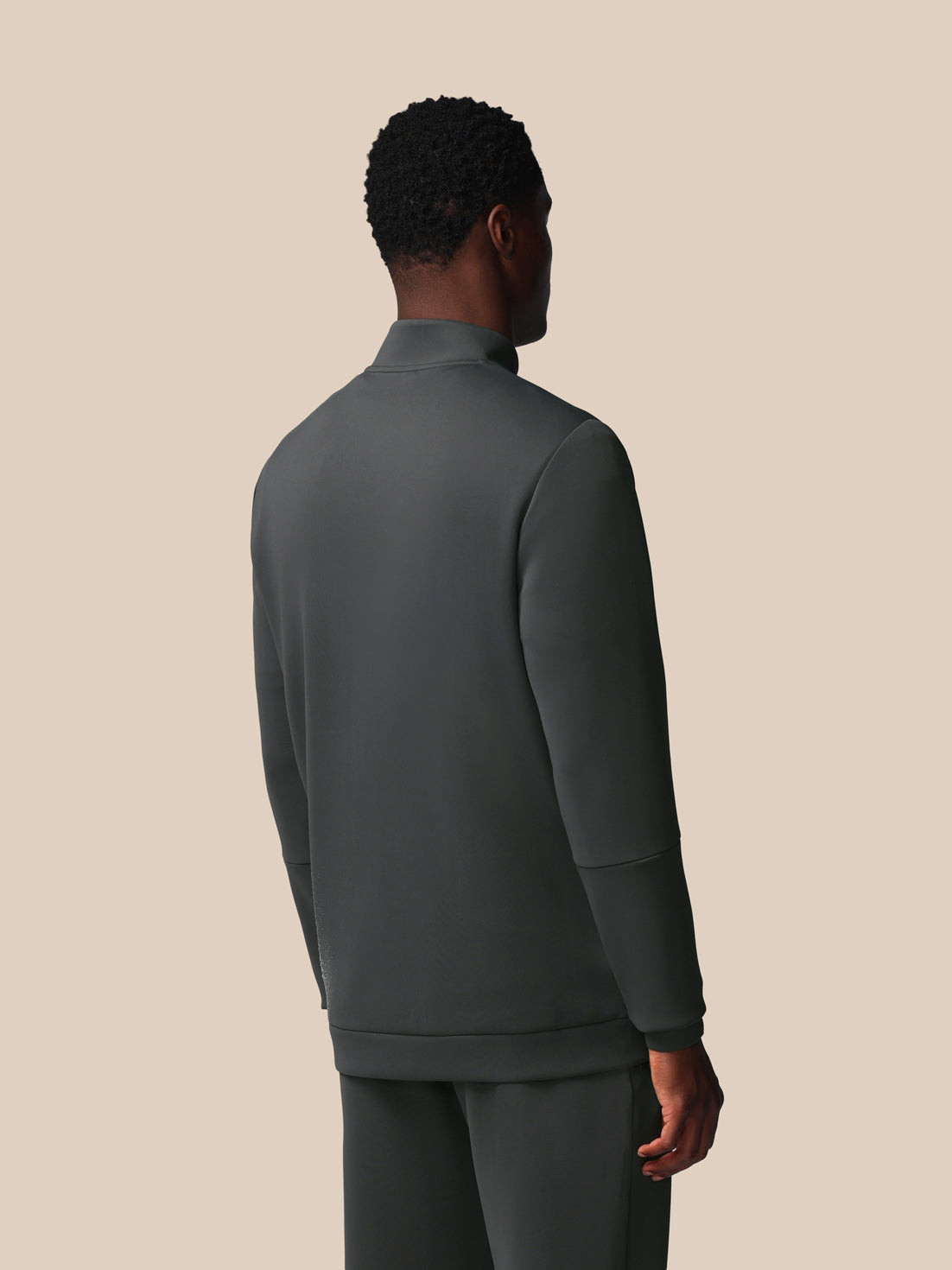 Person wearing a dark gray jacket and pants on a beige background