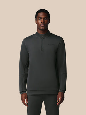 Man wearing a dark gray pullover with a brand logo on a beige background