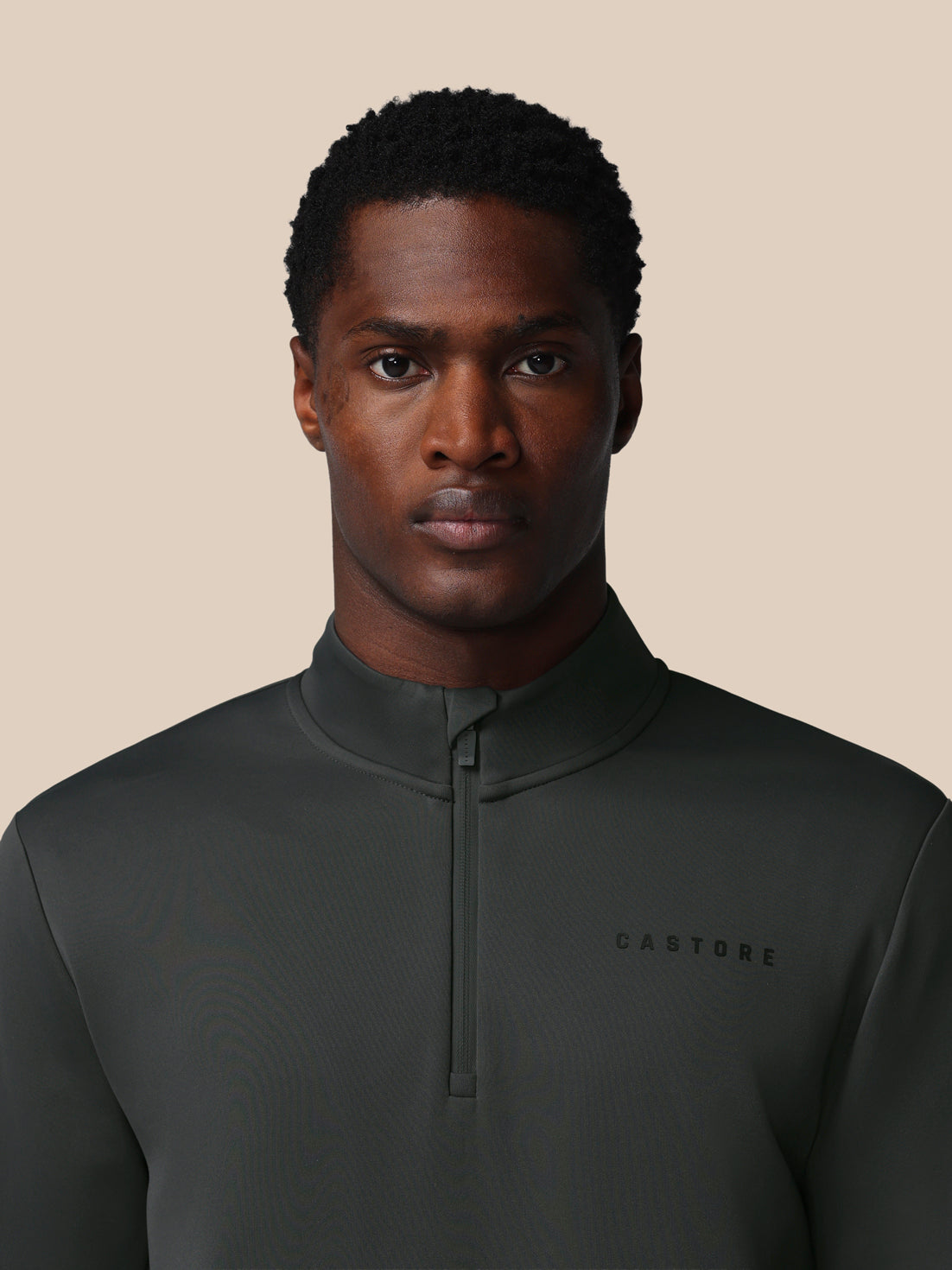 Man wearing a dark green pullover with 'CASTORE' branding on a beige background
